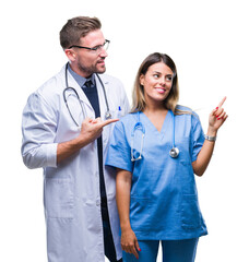 Wall Mural - Young couple of doctor and surgeon over isolated background with a big smile on face, pointing with hand and finger to the side looking at the camera.