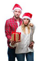 Wall Mural - Young couple in love wearing christmas hat and holding present over isolated background pointing with finger to the camera and to you, hand sign, positive and confident gesture from the front