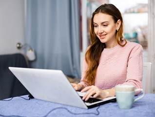 Wall Mural - Portrait of a young woman working on a laptop, sitting at a table in an apartment