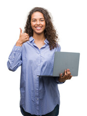 Sticker - Young hispanic woman holding computer laptop happy with big smile doing ok sign, thumb up with fingers, excellent sign