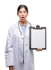 Sticker - Young hispanic doctor woman holding clipboard scared in shock with a surprise face, afraid and excited with fear expression