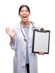 Sticker - Young hispanic doctor woman holding clipboard very happy and excited, winner expression celebrating victory screaming with big smile and raised hands