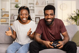 Fototapeta  - Happy Couple Enjoying Video Games Together At Home. Joyful Man And Woman With Game Controller, Casual Clothing, Excitement, Leisure Activity, Gaming Challenge.
