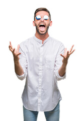 Wall Mural - Young handsome man wearing glasses over isolated background crazy and mad shouting and yelling with aggressive expression and arms raised. Frustration concept.