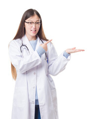 Sticker - Young Chinese doctor woman over isolated background amazed and smiling to the camera while presenting with hand and pointing with finger.