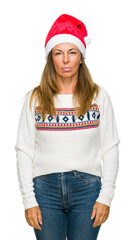 Poster - Middle age adult woman wearing winter sweater and chrismat hat over isolated background with serious expression on face. Simple and natural looking at the camera.