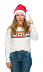 Wall Mural - Middle age adult woman wearing winter sweater and chrismat hat over isolated background pointing finger up with successful idea. Exited and happy. Number one.