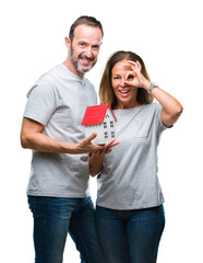 Canvas Print - Middle age hispanic casual couple buying new house over isolated background with happy face smiling doing ok sign with hand on eye looking through fingers