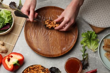 Woman making tasty spring roll at grey table, top view