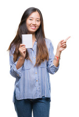 Sticker - Young asian woman holding notebook over isolated background very happy pointing with hand and finger to the side