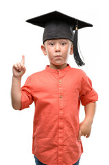 Canvas Print - Dark haired little child wearing graduation cap surprised with an idea or question pointing finger with happy face, number one