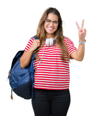 Sticker - Young beautiful brunette student woman wearing headphones and backpack over isolated background smiling with happy face winking at the camera doing victory sign. Number two.