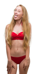 Wall Mural - Blonde teenager woman wearing red bikini sticking tongue out happy with funny expression. Emotion concept.