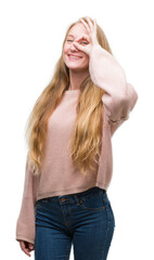 Poster - Blonde teenager woman wearing pink sweater doing ok gesture with hand smiling, eye looking through fingers with happy face.