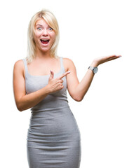 Wall Mural - Young beautiful blonde woman over isolated background amazed and smiling to the camera while presenting with hand and pointing with finger.