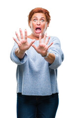 Poster - Atrractive senior caucasian redhead woman wearing winter sweater over isolated background afraid and terrified with fear expression stop gesture with hands, shouting in shock. Panic concept.