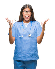 Wall Mural - Young asian doctor woman over isolated background celebrating crazy and amazed for success with arms raised and open eyes screaming excited. Winner concept