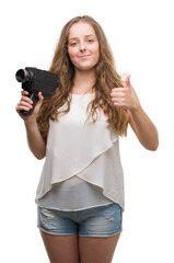 Poster - Young blonde woman holding super 8 video camera happy with big smile doing ok sign, thumb up with fingers, excellent sign