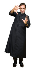 Sticker - Middle age priest man wearing catholic robe Smiling doing frame using hands palms and fingers, camera perspective