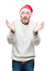 Wall Mural - Middle age hoary senior man wearing christmas hat over isolated background clueless and confused expression with arms and hands raised. Doubt concept.