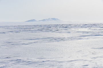 Wall Mural - Arctic landscape. View of snow-covered tundra. In the distance are snow-capped mountains. White silence. Cold weather in April. The harsh climate and nature of the polar region. Arctic desert.