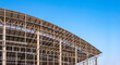 Part of large metal industrial factory building structure with corrugated steel curve roof and skylights in construction site against blue sky background, low angle view with copy space