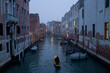 A boat in a canal of Venice at dusk.