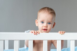 Fototapeta Miasto - The baby is surprised and pulls himself up on the back of the crib with little effort