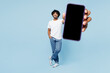 © ViDi Studio - Full body young happy Indian man wear white t-shirt casual clothes hold in hand use blank screen workspace area mobile cell phone isolated on plain pastel light blue cyan background Lifestyle concept
