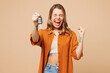 Young happy woman she wears orange shirt casual clothes hold in hand car keys fob keyless system do winner gesture isolated on plain pastel light beige background studio portrait. Lifestyle concept.