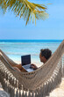 © Song_about_summer - digital nomad, man working on laptop from hammock on the beach, dream job