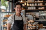 Fototapeta  - Happy young asian male cafe owner standing at the counter in front of the display window, smiling and looking directly at the camera. generative AI