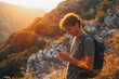 Handsome young man looking and smiling at the phone at sunset in the mountains