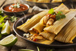 A close-up shot of a plate of tamales, carefully unwrapped from their corn husk casings to reveal the steaming, moist masa filled with a rich and savory mixture of chicken and green salsa.
