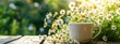 A cup of chamomile tea with a fresh bouquet of chamomile flowers on a wooden table. Blurred background with garden.