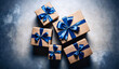 From above five rustic brown paper holiday gift boxes in different sizes with blue ribbon and bow on concrete grey and dark blue background