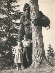 Old vintage aged mystery photograph of a man and woman standing with a giant bigfoot cryptid sasquatch creature in the forest