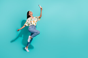 Poster - Full length photo of cheerful charming girl blogger walking and speaking video chat running empty space isolated on cyan color background