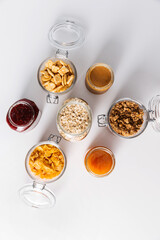 Wall Mural - food storage and eating concept - close up of jars with oat, corn flakes, granola, cookies and spreads on white background