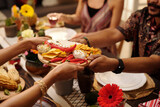 Fototapeta  - Hands of young woman passing tray with nachos, red hot chili peppers and savory sauce to male guest sitting by served festive table
