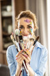 Portrait of a cute Latin woman holding a bunch of paintbrushes with both hands and smiling