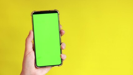 Chroma key mockup on smartphone in hand. Showcasing copy space for app or website design. A woman is holding a smartphone with a blank green screen on a yellow background