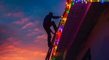 A Man Climbs A Ladder Adorned With Christmas Lights To Install Them On The Eaves