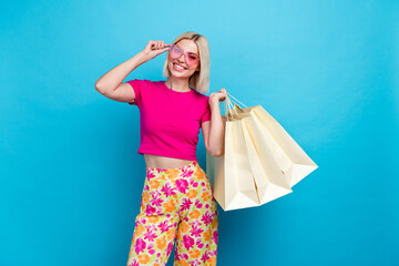 Sticker - Photo portrait of attractive young woman sunglass hold shopping bags dressed stylish pink clothes isolated on blue color background.