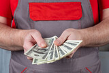 Fototapeta Desenie - A man in work clothes holds a stack of 100 dollar bills in his hands.