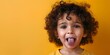 Playful Child Sticking Out Tongue in Defiant Display with Curly Hair and Vibrant Yellow Background