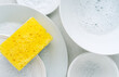 Yellow sponge and a soapy foam, white plate with soap suds on a background. Cleaning concept, cleaning service, flat lay, top view