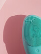 Silicone brush for washing face. Blue facial cleansing brush on pink background. Skincare and Beauty concept. Brush for face massage, lifting, anti-aging wrinkles.