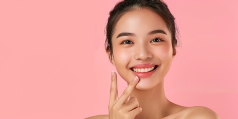 Beautiful young Asian woman pointing finger to her teeth on pink background. Facial and skin care concept for commercial advertising.