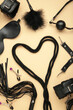 BDSM set on beige background. BDSM accessories and rope in the shape of a heart. Mask, handcuffs, ball gag and a whip. Vertical photo